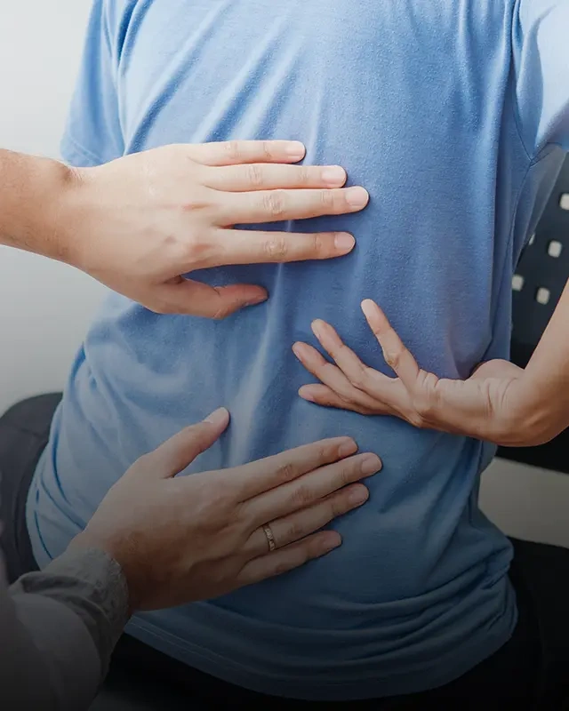 Close-up of three hands gently pressing and supporting a person’s back, who is wearing a blue shirt, during a chiropractic or physical therapy session