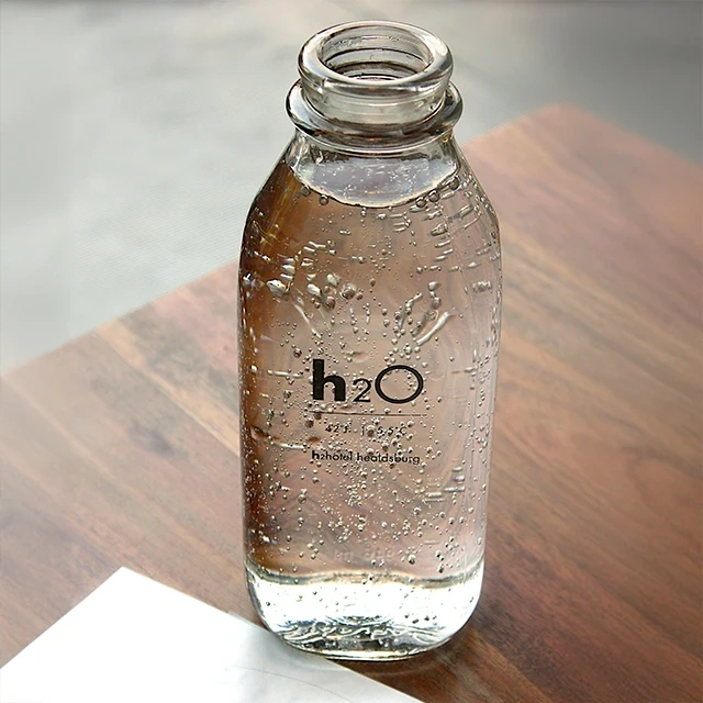 Clear glass bottle filled with sparkling water, labeled ‘h2O’, placed on a wooden surface
