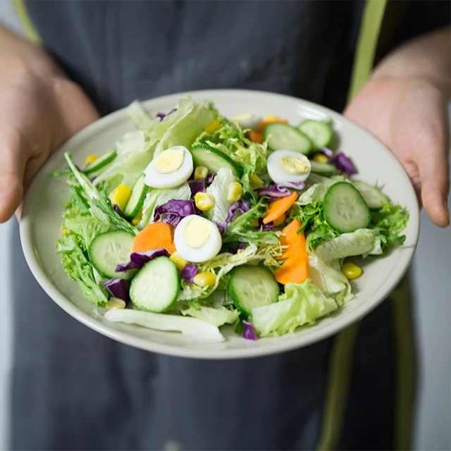 Plate of fresh salad with sliced cucumbers, boiled egg slices, lettuce, shredded purple cabbage, carrot pieces, and corn kernels