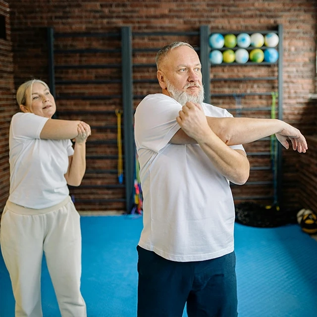 Two people performing arm stretches in a fitness studio with blue flooring