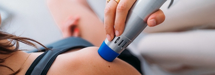 Close-up of a person receiving Low Level Laser Therapy therapy on the shoulder using a handheld device with a blue applicator tip