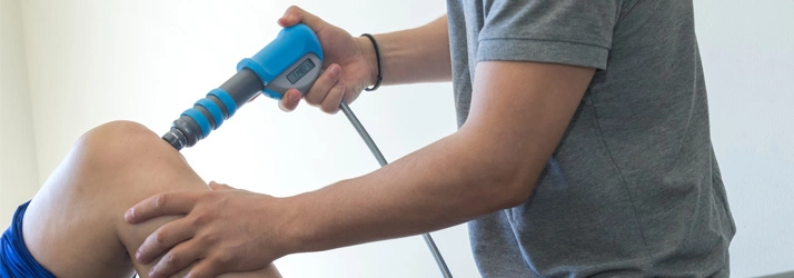 Person performing shockwave therapy on a knee using a blue handheld device